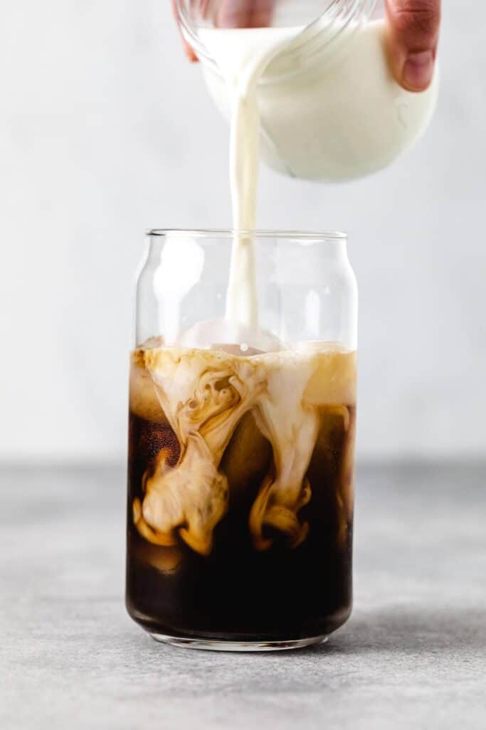 A person pouring milk in the cup of coffee 