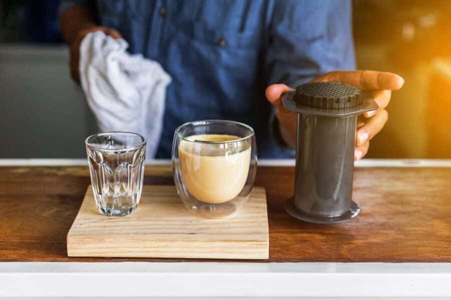 someone making aeropress latte a galss mug and aeropress machine placed on the table