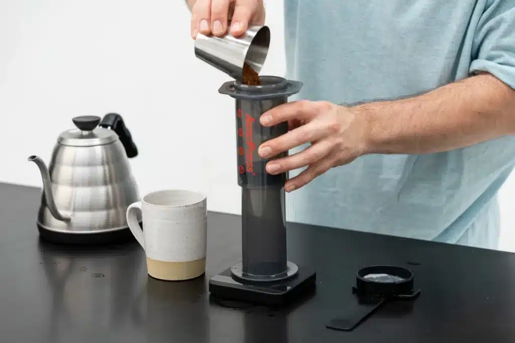 someone making coffee using an inverted method on an aeropress machine a mug and kettle on the table