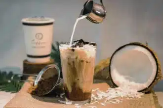 a person adding milk to the coconut coffee, with coconut placed on side