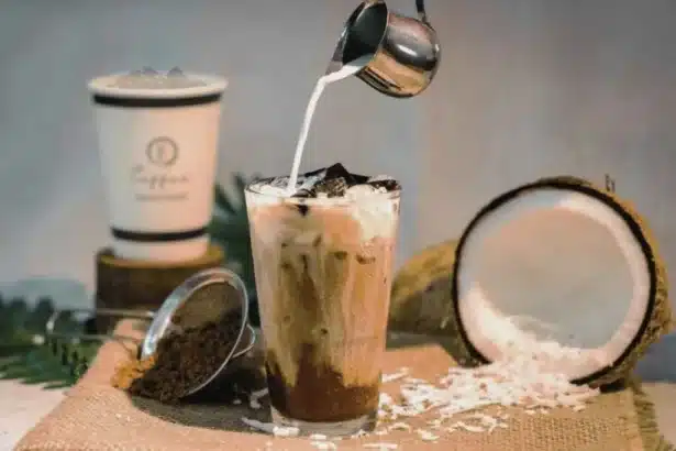 a person adding milk to the coconut coffee, with coconut placed on side