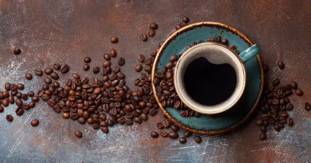 a cup of coffee in a saucer coffee beans spilled around on a surface