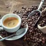 a cup of red eye coffee placed on a plate with a spoon coffee beans scattered on a surface