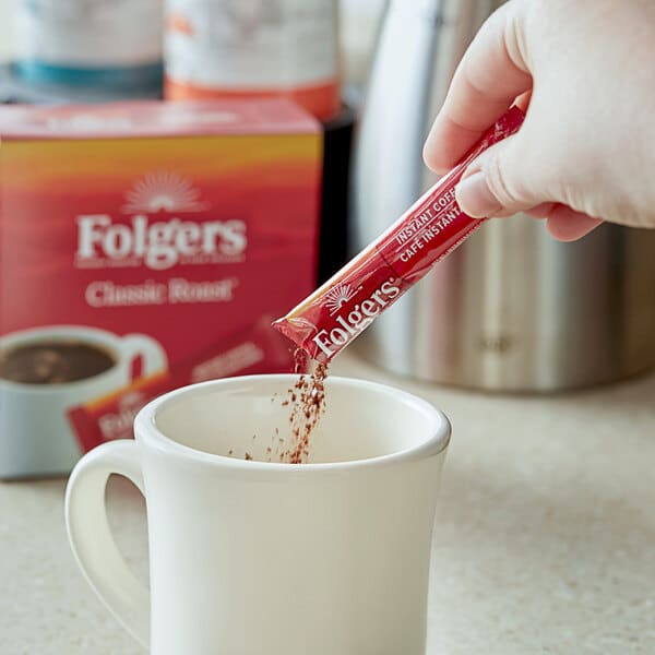 a hand pouring instant coffee in a white mug