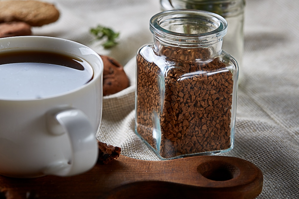 a white mug of coffee a jar of coffee granules placed on a fabric