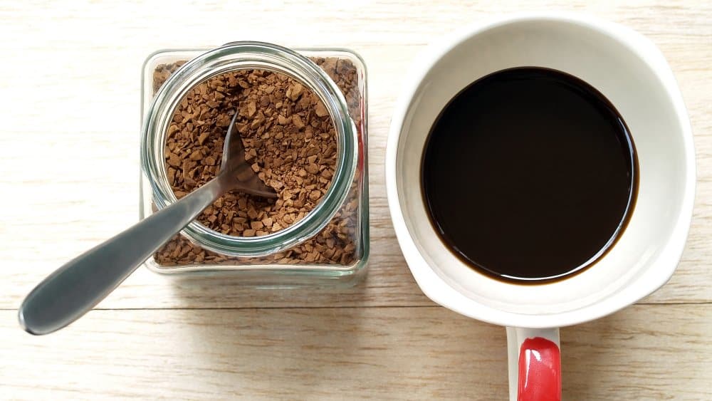 instant coffee in amug jar of coffee with a spoon placed on a wooden surface