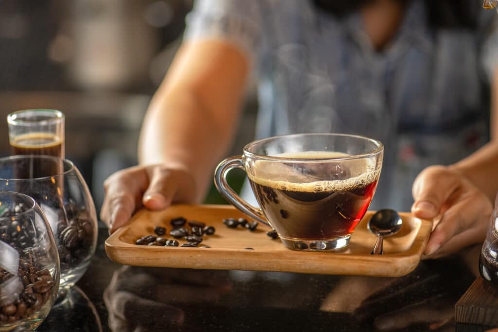 male hands handing a tray with a cup of red coffee in a cup a spoon placed on the side