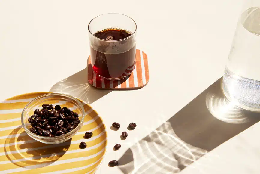 coffee beans in a small bowl coffeee in a small glass and half cut view of water jug