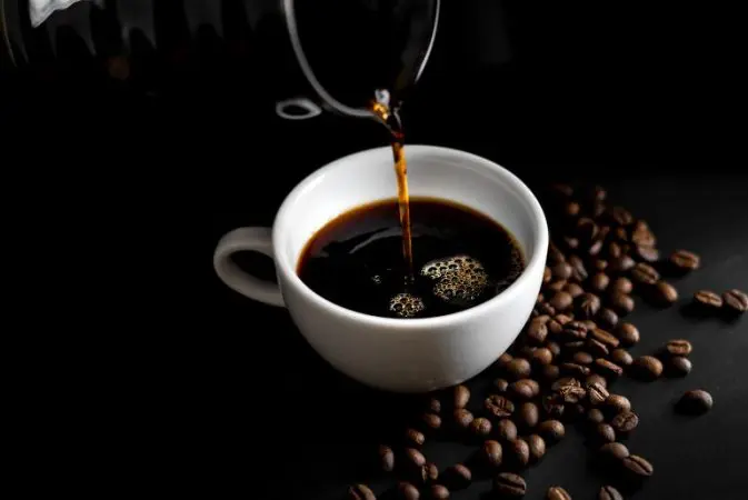 coffee dripping in white cup beans dispersed around