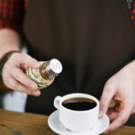 Hands of barista adding salt in black coffee