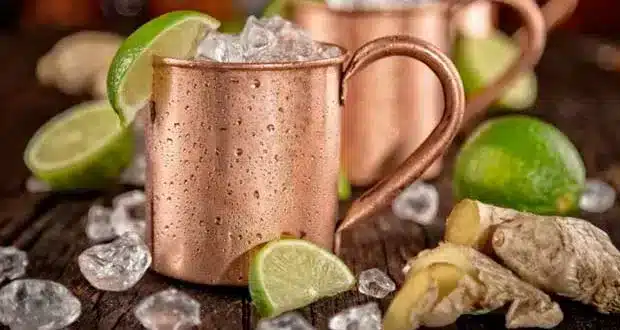 a cup of Coffee Mule  garnished with lemon wedges and ginger