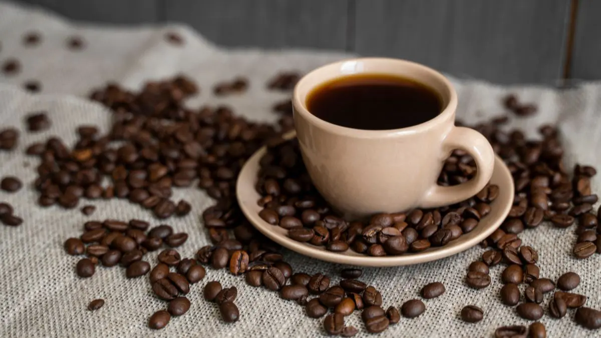 a cup of black eye coffee placed on a saucer and coffee beans around