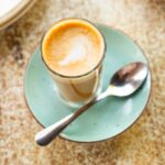 cortado drink in a cup placed on a plate with a spoon