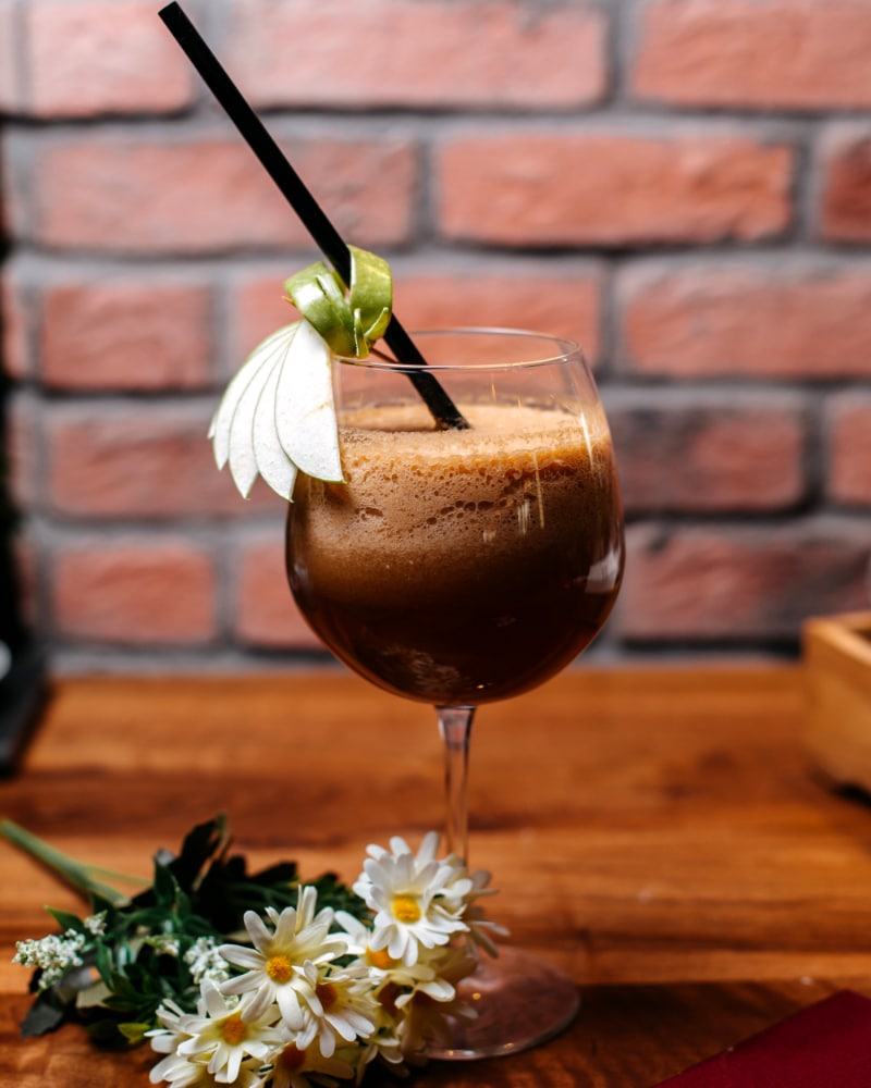 a glass of black russian coffee with a straw inside and a bouqet of flowers placed nearby