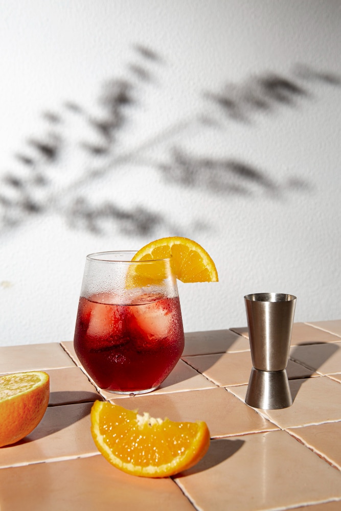 a glass of cold brew negroni garnished with an oraange wedge and a slice of orange placed nearby