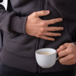 Man Suffering From Stomach Pain With Cup Of Coffee