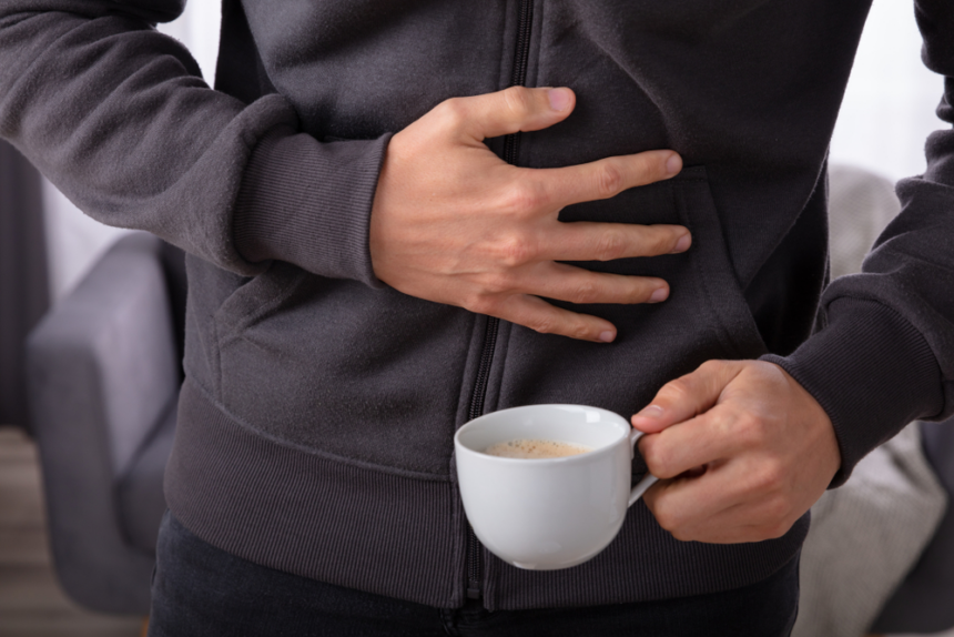 Man Suffering From Stomach Pain With Cup Of Coffee