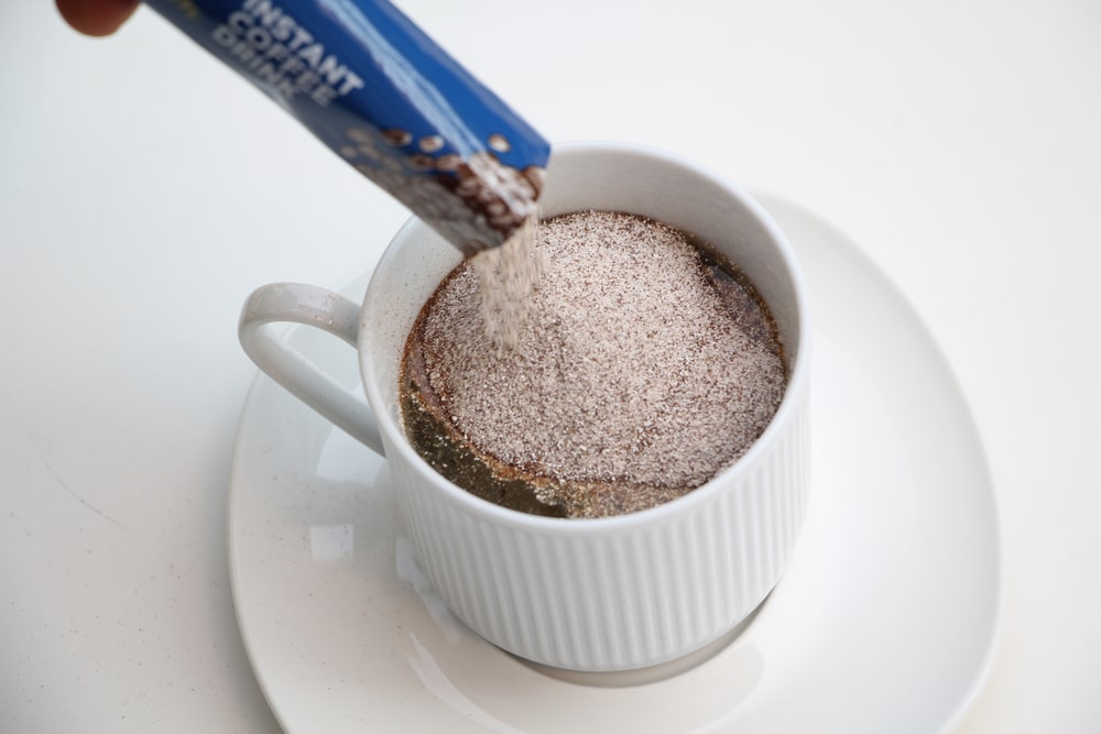 Instant coffee is poured into a white coffee cup with hot water